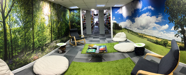 Shows the relaxation room at the Arts and Social Sciences Library. It has soft seating, green carpets and woodland and field wallpaper